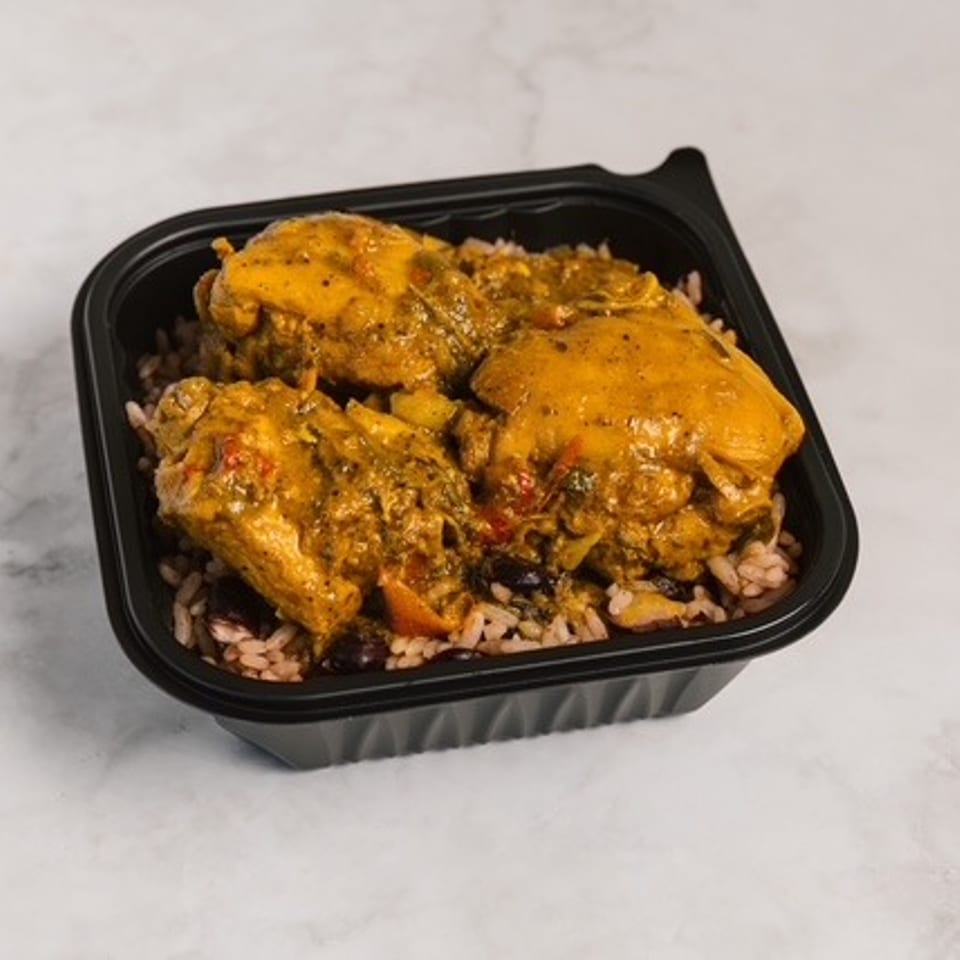 Black takeout container holding spiced chicken pieces over rice and beans on a white marble surface.