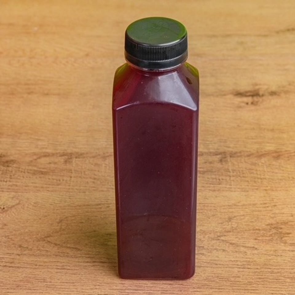 Square bottle filled with dark red beverage and capped with a black lid, standing on a wooden table.